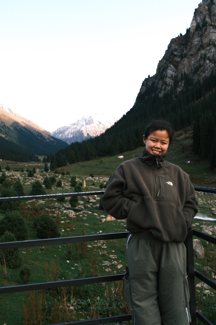 Mandy standing at a railing on an alpine platform, with a valley and mountain peaks behind her